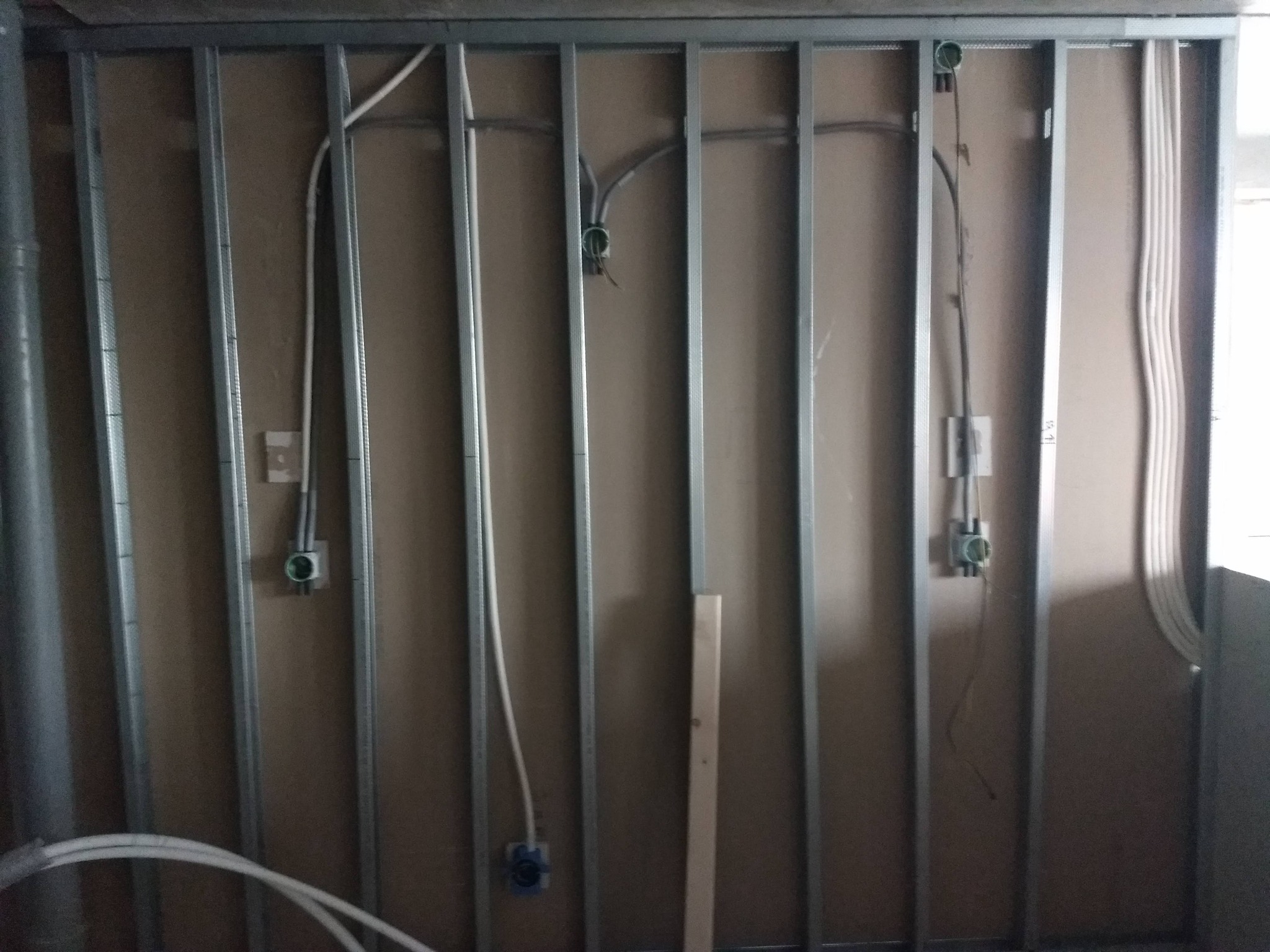 Konstrukcja ściany z profili stalowych, obłożona płytami kartonowo-gipsowymi z widocznymi przewodami elektrycznymi i puszkami instalacyjnymi w trakcie montażu.