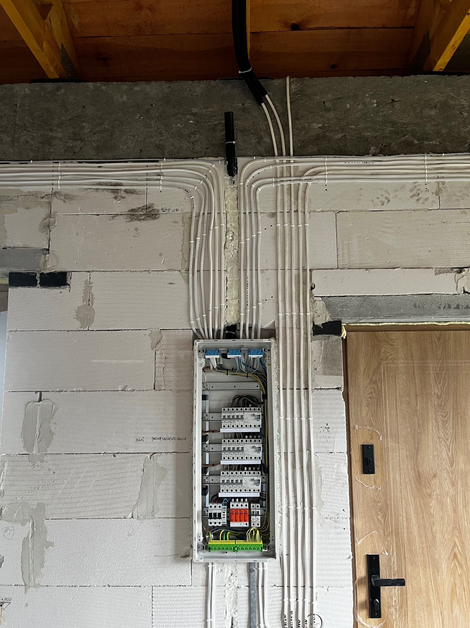 Rozdzielnica elektryczna z licznymi przewodami ułożonymi równolegle na ścianie z betonu komórkowego, widoczne zabezpieczenia i złącza. Estetyczne wykonanie instalacji.