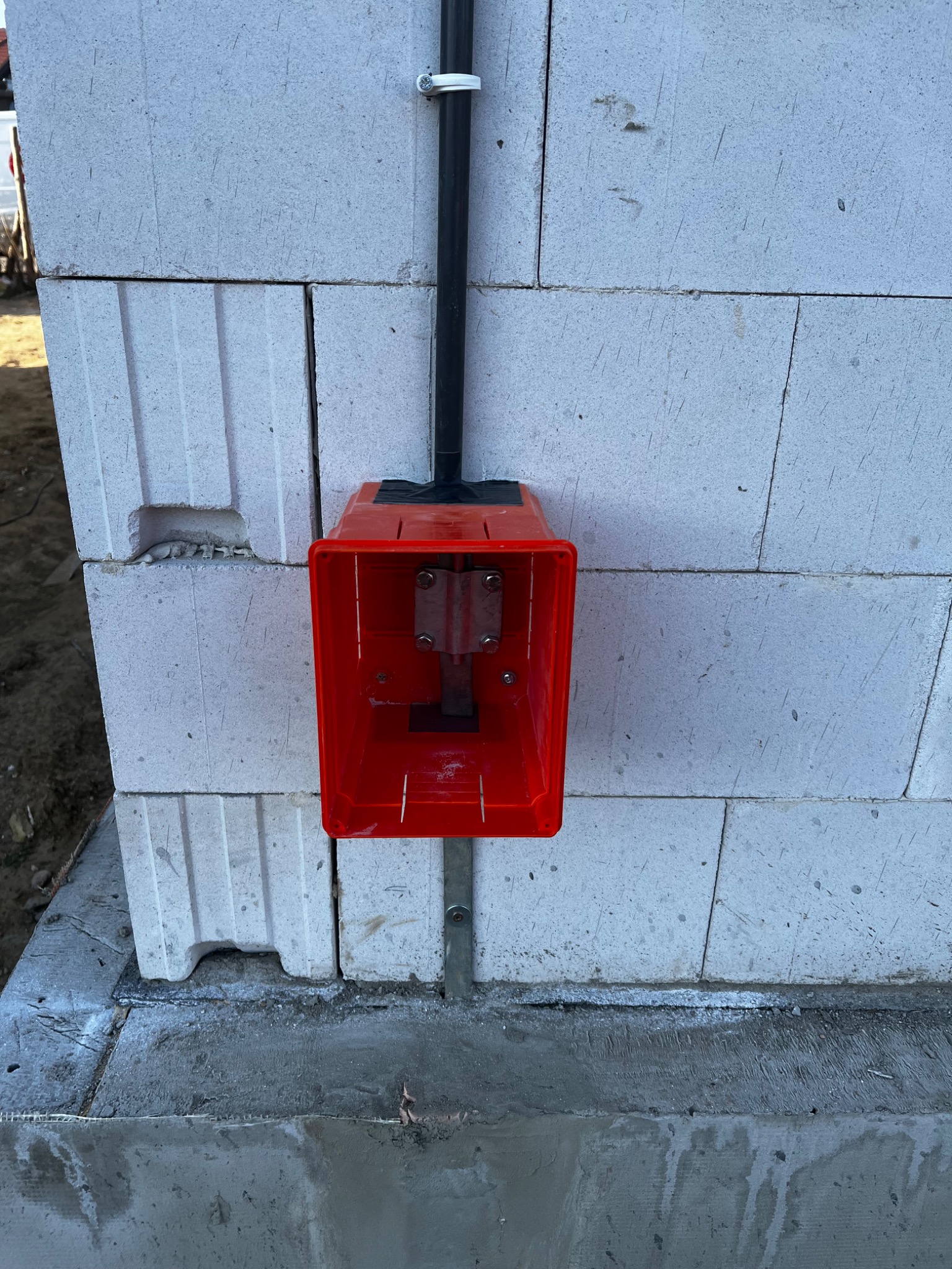 Czerwona puszka instalacyjna zamontowana na ścianie z betonu komórkowego, z widocznym przewodem w peszlu. Instalacja w trakcie budowy.