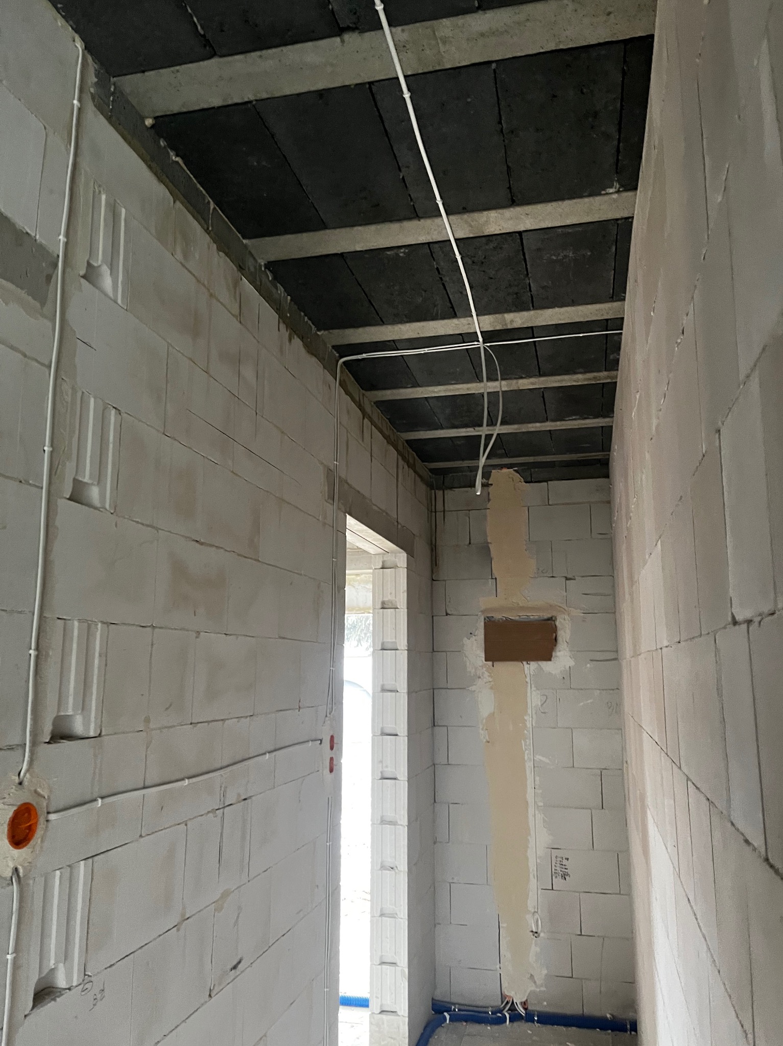 Wnętrze w trakcie prac instalacyjnych: białe ściany z betonu komórkowego, widoczne przewody elektryczne prowadzone po ścianach i pod sufitem, otwór w ścianie przygotowany pod instalację.