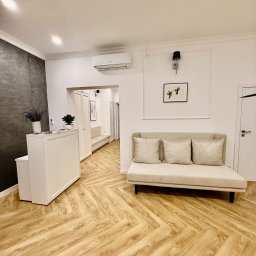 CENTRUM WSPARCIA DOBROSTAN SPÓŁKA Z OGRANICZONĄ ODPOWIEDZIALNOŚCIĄ - Jasne wnętrze poczekalni z recepcją, sofą z poduszkami i wzorzystą podłogą z paneli, widok na korytarz z drzwiami i schodami.