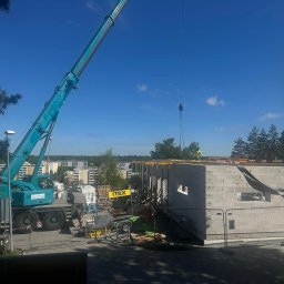 4U SOLUTION SPÓŁKA Z OGRANICZONĄ ODPOWIEDZIALNOŚCIĄ - Budowa budynku z bloczków betonowych z użyciem dźwigu, widoczne szalunki i pracownik w żółtym ubraniu na dachu.