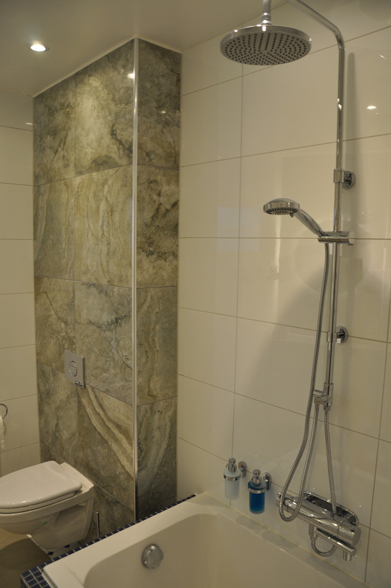 Nowoczesna łazienka z kabiną prysznicową typu deszczownica, obudowana płytkami imitującymi marmur, biała armatura i minimalistyczne dodatki.