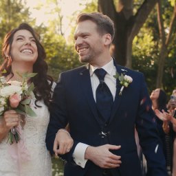 RUSLAN BURMISTROV - Uśmiechnięta para młoda, idąca alejką w otoczeniu gości, z konfetti opadającym z góry podczas ceremonii ślubnej w plenerze.