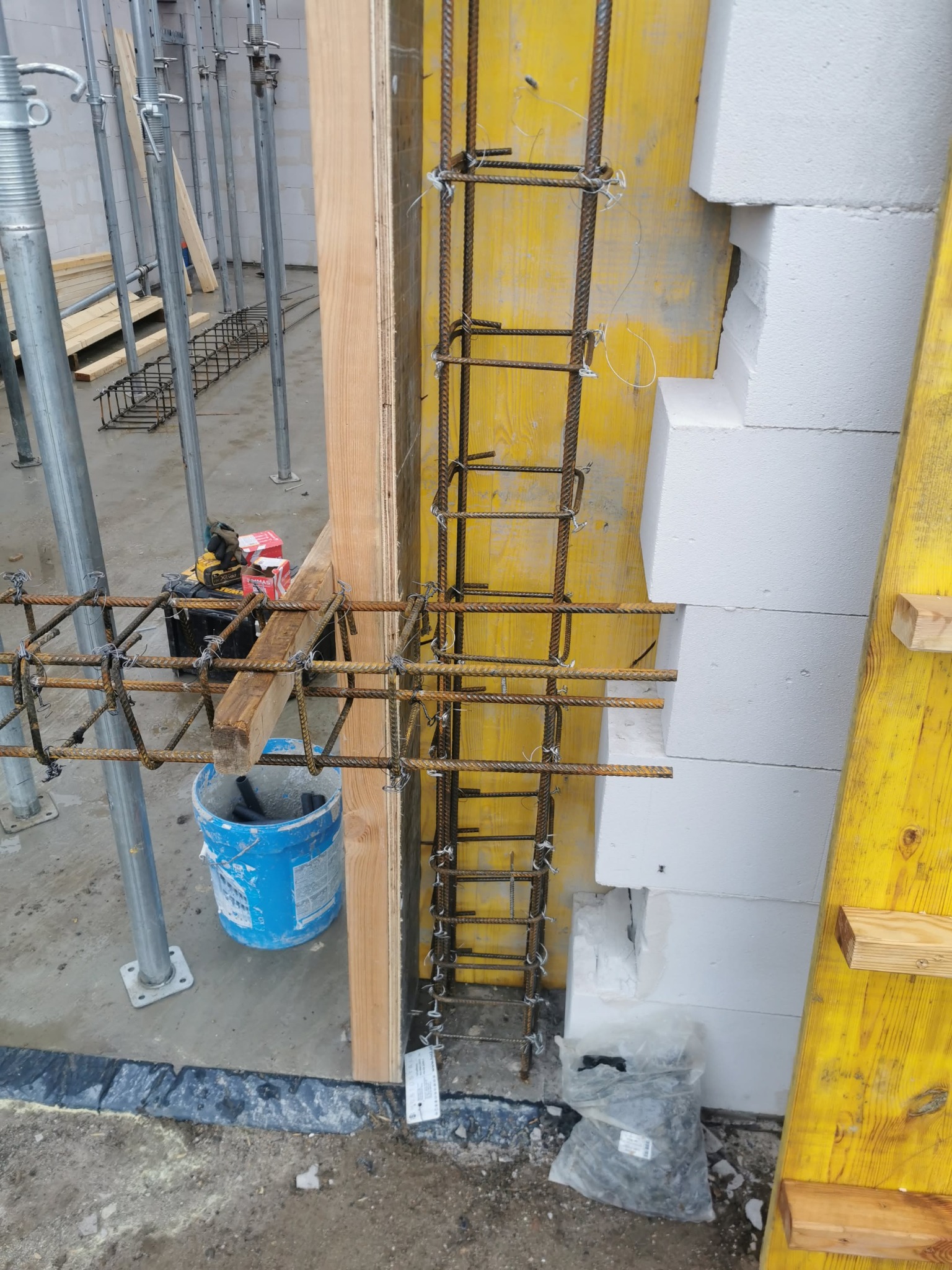 Zbrojenie pionowe i poziome w szalunku, białe bloczki Ytong, podpory budowlane. Etap budowy domu z betonu komórkowego.