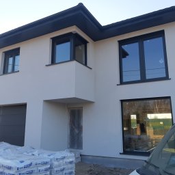 BARTOR - Nowoczesny dom jednorodzinny z jasną elewacją, grafitową stolarką okienną i stosem worków z zaprawą gipsową Knauf MP 75 Diamant przed wejściem, zabezpieczonym folią.