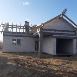 BARTOR - Surowy stan budynku jednorodzinnego z białych bloczków, w trakcie budowy dachu, z małą choinką na szczycie, na tle błękitnego nieba.