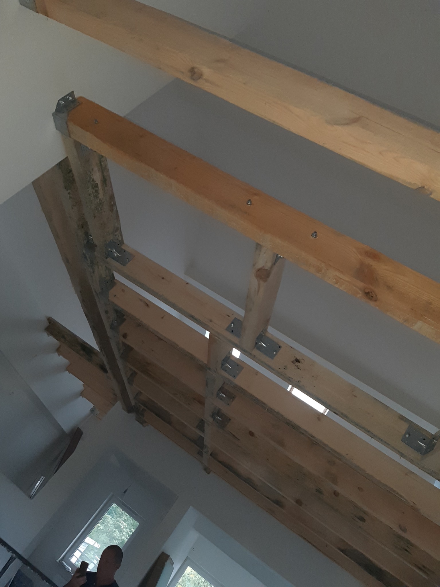 Drewniana konstrukcja więźby dachowej z metalowymi łącznikami, widok od dołu, fragment poddasza z oknami.