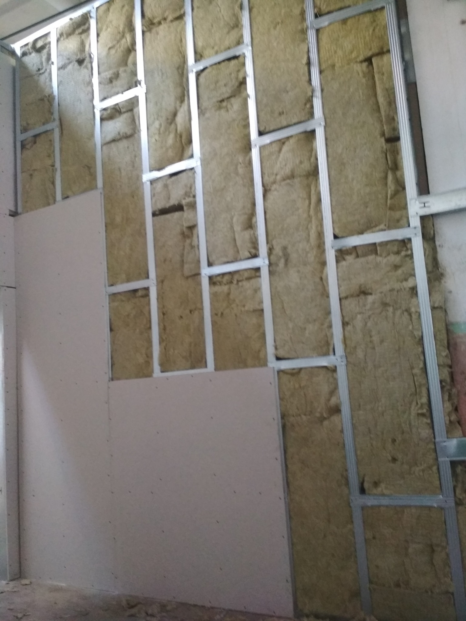 Konstrukcja metalowa z izolacją z wełny mineralnej, częściowo zakryta płytami gipsowo-kartonowymi, widoczne ślady montażu na płytach.