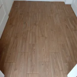 Ułożone panele podłogowe imitujące drewno w wąskim korytarzu, widoczne białe futryny drzwiowe i listwa progowa.