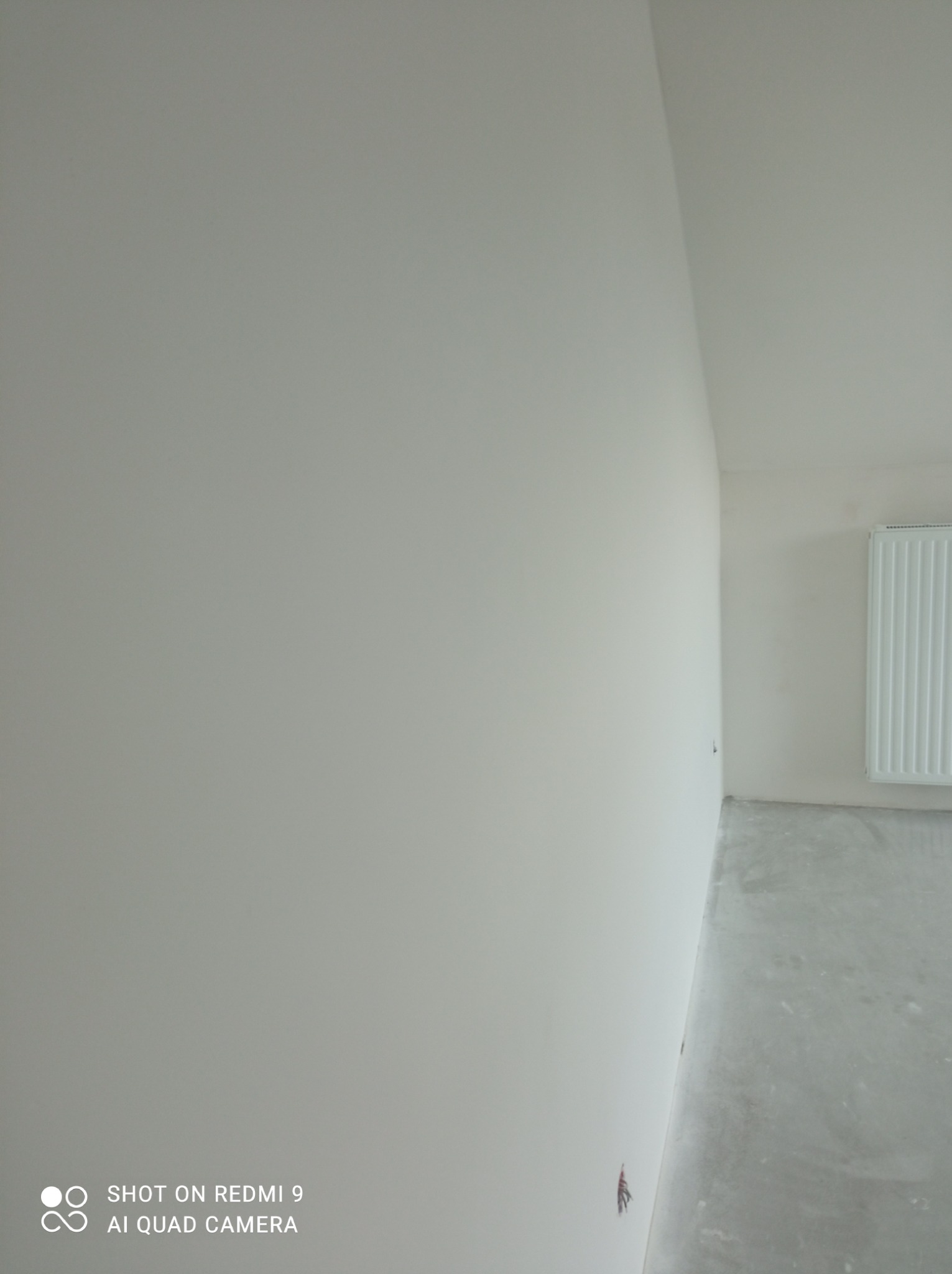 Świeżo pomalowane na biało wnętrze z grzejnikiem, widok z dołu ukazujący gładką powierzchnię ścian i sufitu oraz szary betonowy podkład pod podłogę.