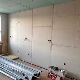 VRWOLT - Usługi Elektryczne - Wnętrze w trakcie remontu: ściany i sufit pokryte płytami gipsowo-kartonowymi, widoczne kable elektryczne wystające ze ścian, profile metalowe na podłodze.