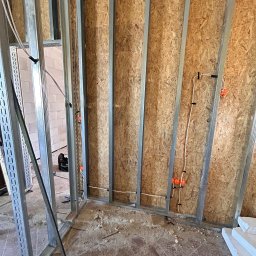 VRWOLT - Usługi Elektryczne - Wewnętrzna instalacja elektryczna w ścianie szkieletowej z widocznymi przewodami i puszkami. Etap prac przed wykończeniem, widoczne płyty OSB i metalowe profile.