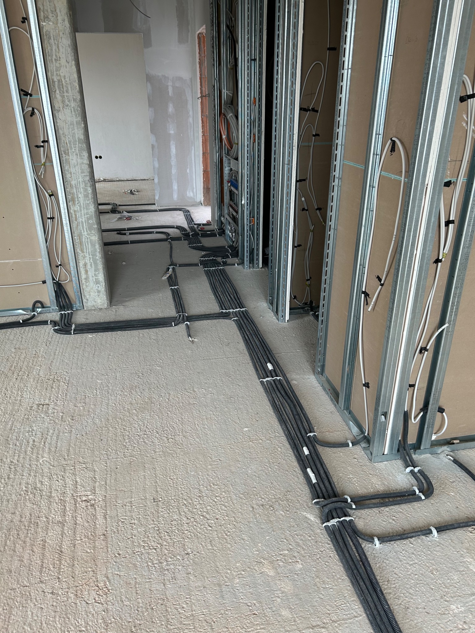 Rozprowadzone kable elektryczne w peszlach, przymocowane do podłoża i ścian w surowym stanie, widoczne metalowe profile konstrukcyjne ścian działowych.