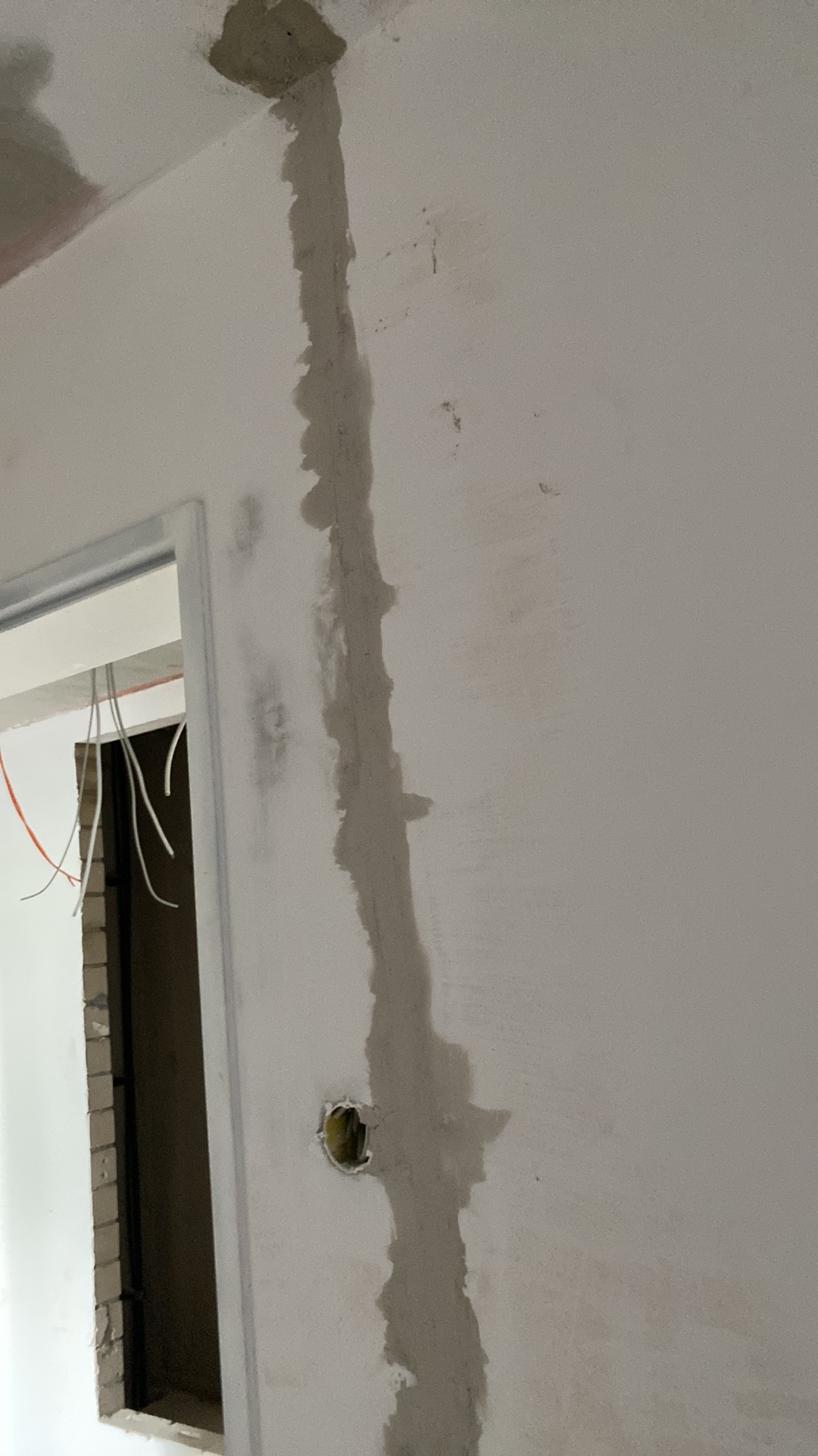 Świeżo położona gładź maskuje przewody elektryczne w ścianie, widoczne kable w otworze pod gniazdko i fragment futryny drzwiowej.