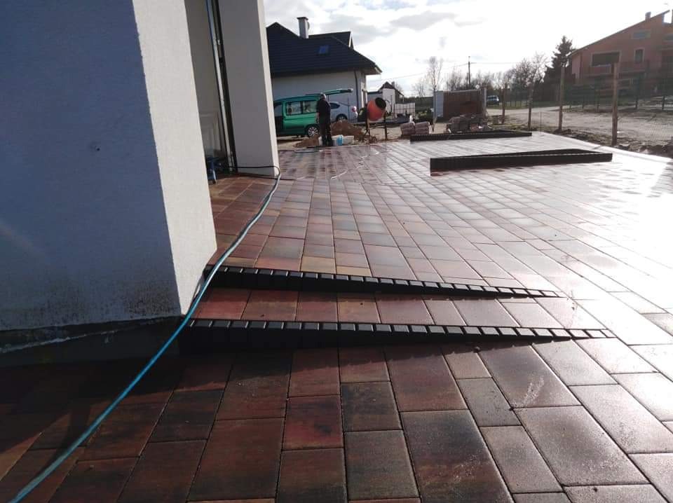 Nowo ułożona, mokra, wielobarwna kostka brukowa prowadząca do domu z dwoma stopniami, widoczny mikser budowlany w tle.