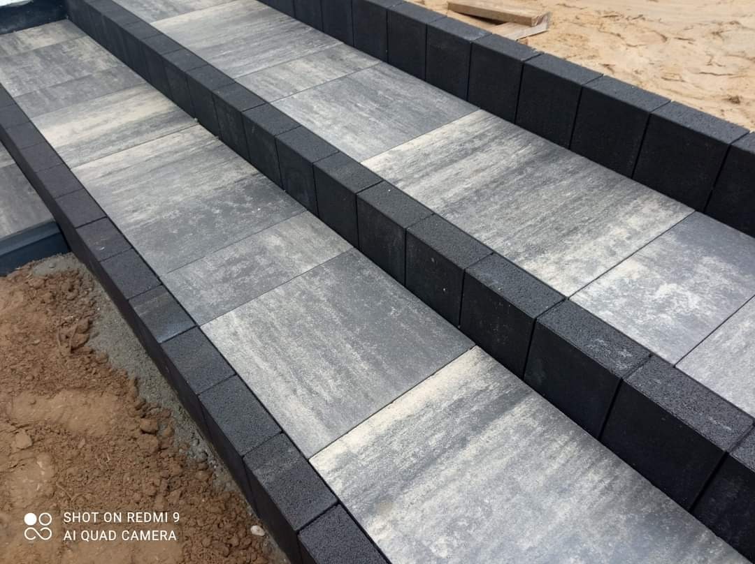 Schody z szarej kostki brukowej z czarnym obrzeżem, widok z góry, częściowo ułożone w piasku.