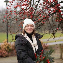 Olena Dankiv - Portret uśmiechniętej kobiety w zimowej stylizacji z bukietem z gałązek i czerwonych jagód na tle drzewa z czerwonymi owocami w Grodzisku Mazowieckim.