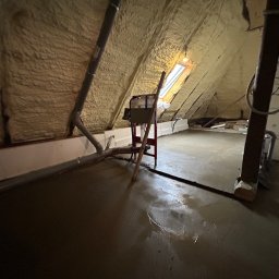 DAW-MAT Dawid Hanuszek - Poddasze w Krzczonowie w trakcie izolacji pianą PUR, widoczna warstwa piany na skosach dachu, rury wentylacyjne i mokra wylewka na podłodze.