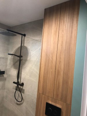 Nowoczesna łazienka z drewnianą szafą w zabudowie, czarna armatura prysznicowa na tle marmurowej ściany, minimalistyczny design.