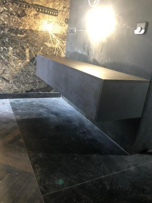 Nowoczesna, podwieszana szafka w łazience z ciemnymi płytkami i dekoracyjną tapetą.