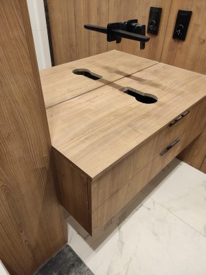 Drewniana szafka pod umywalkę z dwoma szufladami i czarną armaturą, zamontowana na ścianie w łazience z marmurową podłogą.