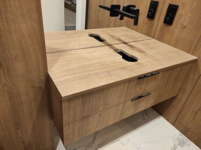 Drewniana szafka z dwiema szufladami i otworami na blacie, zamontowana na ścianie z panelami w tym samym odcieniu drewna.