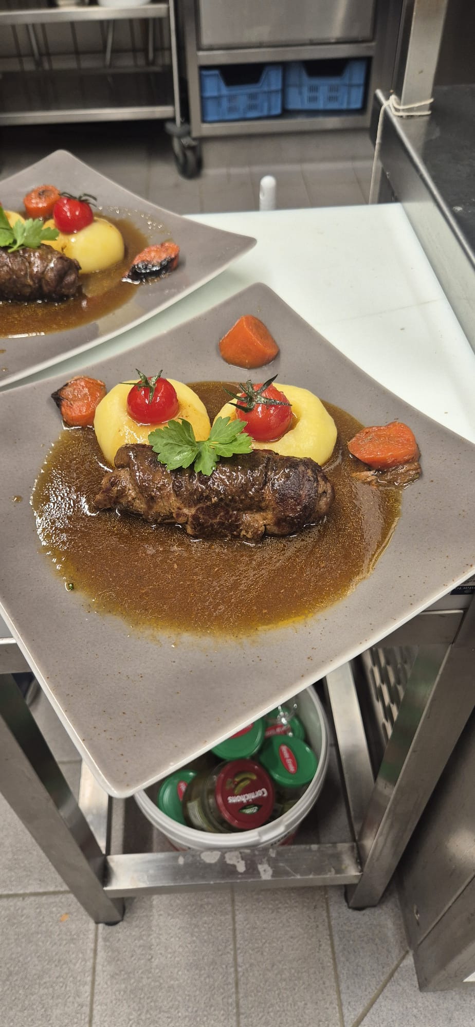 Danie główne: rolada wołowa w sosie własnym, podana na puree ziemniaczanym z pomidorkami cherry i marchewką, na kwadratowym talerzu w kuchni gastronomicznej.