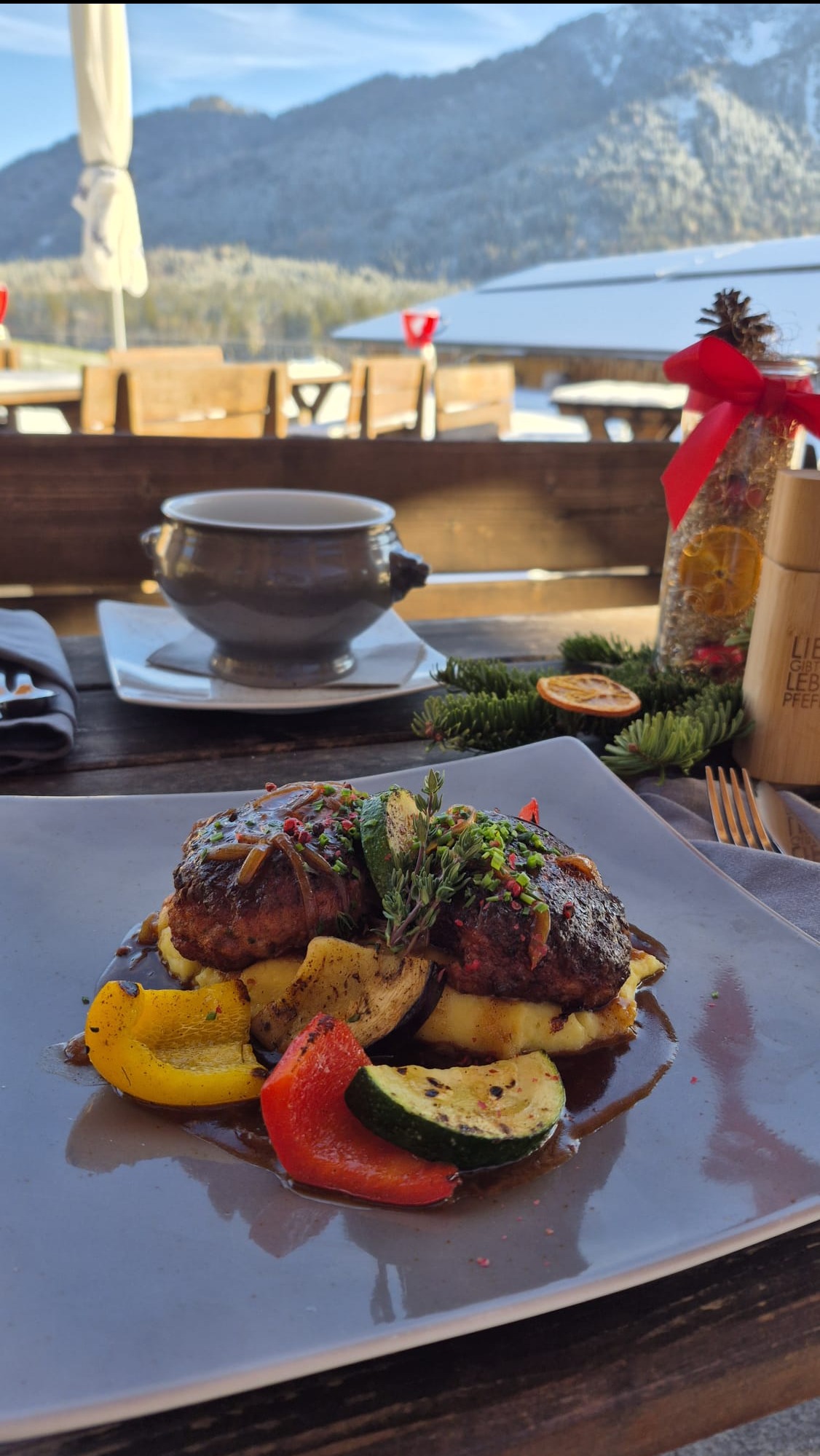 Elegancko podane danie mięsne z warzywami i sosem na talerzu, z zupą w tle i zimowym krajobrazem za oknem.