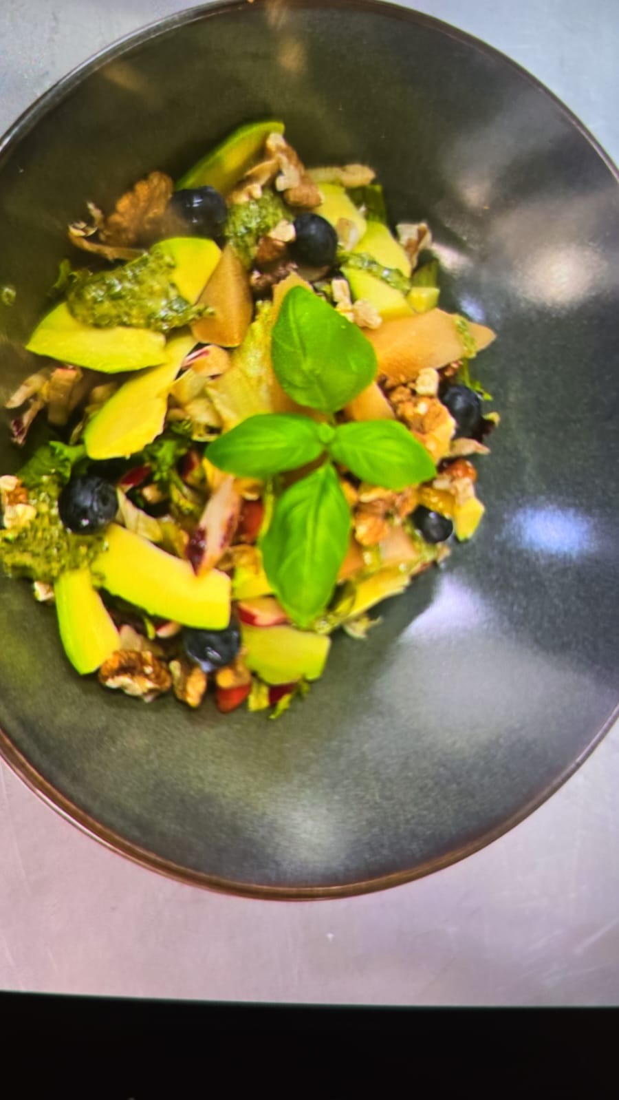 Sałatka z awokado, orzechów włoskich, borówek i listków bazylii w ciemnej, głębokiej misce.