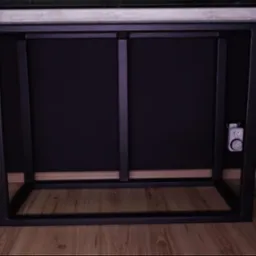 Stół z blatem imitującym beton i metalową ramą, z widocznym programatorem czasowym na nodze, stojący na drewnianej podłodze obok rośliny doniczkowej na tle ciemnej ściany.