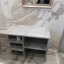 Piotr Benedyk - Wykończona łazienka z marmurowymi ścianami, podłogą i półką, widoczne odbicie osoby w lustrze.