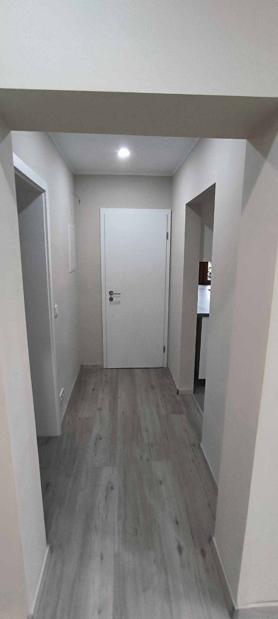Korytarz po remoncie z szarą podłogą imitującą drewno, białe ściany i białe drzwi, widok w głąb mieszkania.