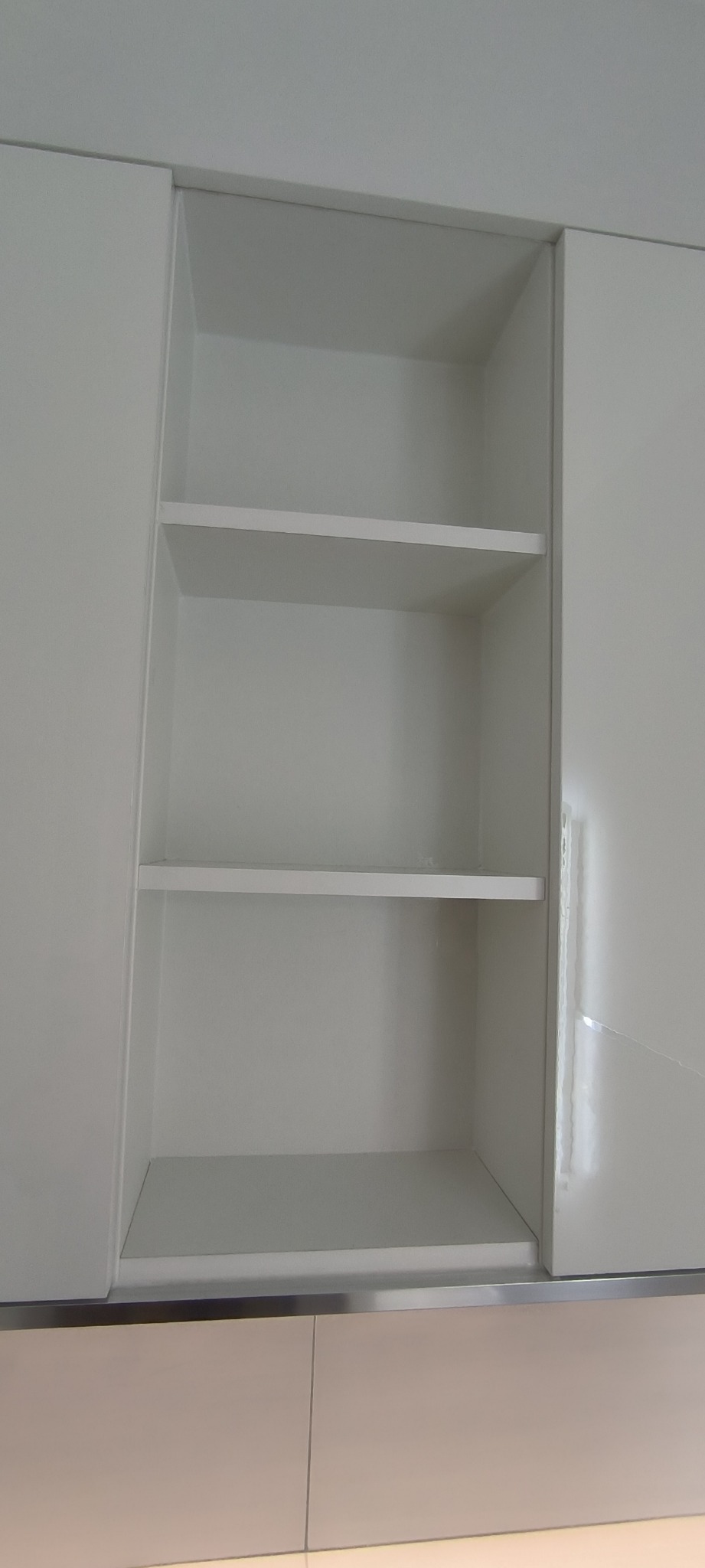 Biała, pusta szafka łazienkowa z trzema półkami, widok z bliska, błyszczące fronty.