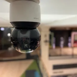 Kamera kopułkowa Wisenet zamontowana na suficie w centrum handlowym, widoczna z dołu, z odbiciem otoczenia w obiektywie.