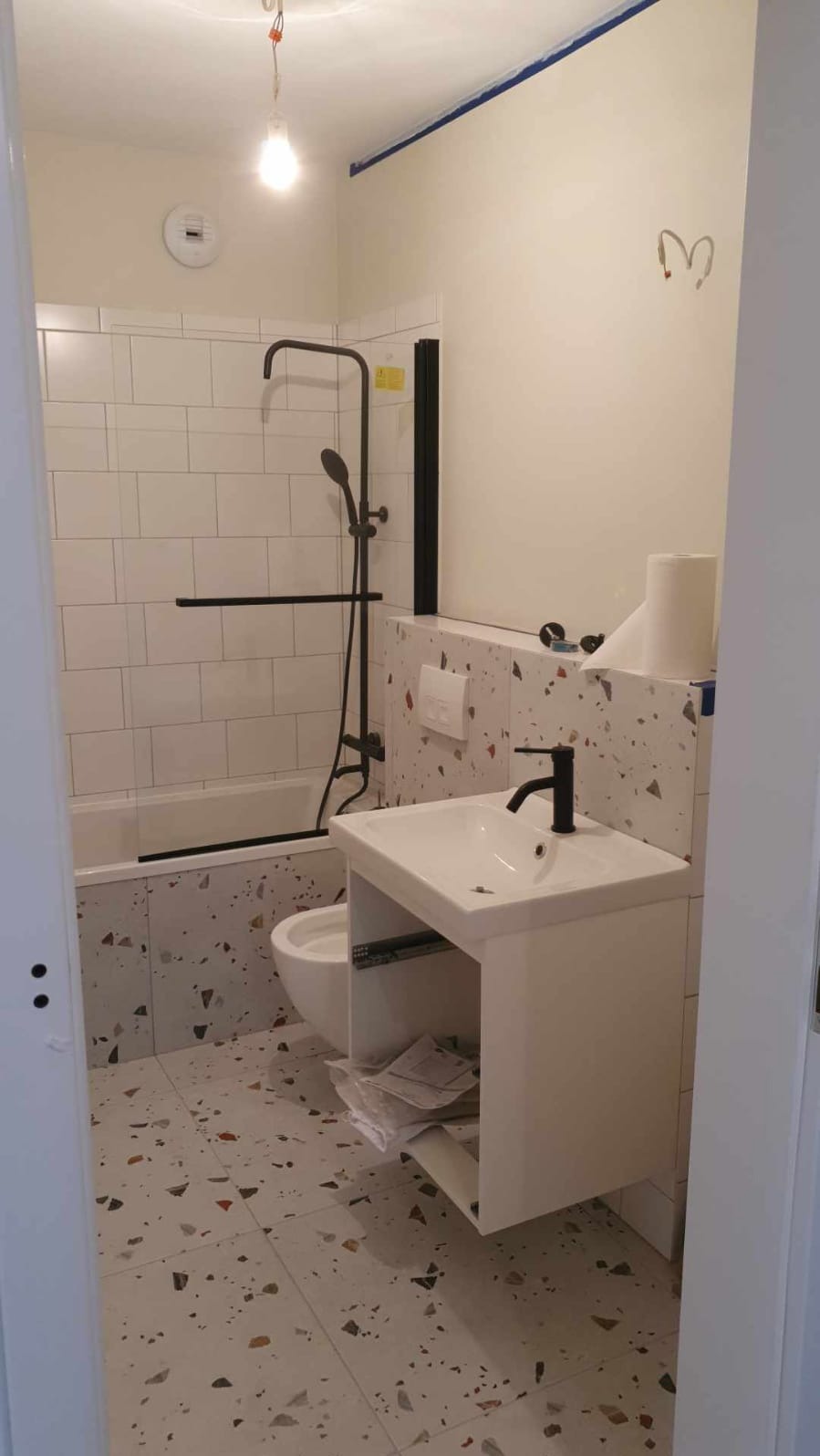 Nowoczesna łazienka z wanną z czarną armaturą, umywalką na szafce i płytkami lastryko na podłodze i ścianach, widoczne ślady prac wykończeniowych.