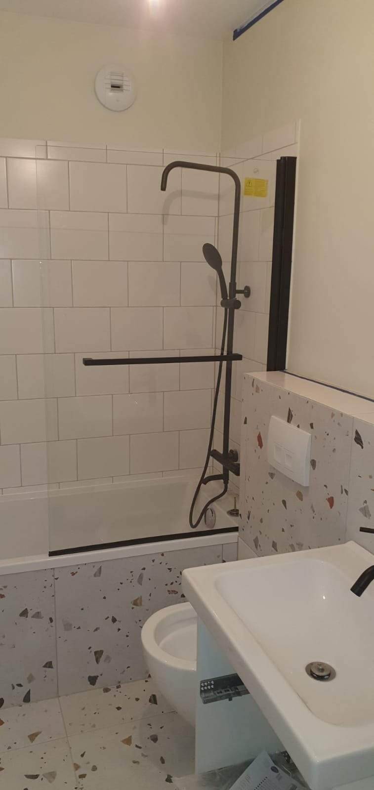 Nowoczesna łazienka w Chorzowie po remoncie, z kabiną prysznicową typu walk-in z czarnymi elementami, białą armaturą i płytkami lastryko na podłodze i części ścian.