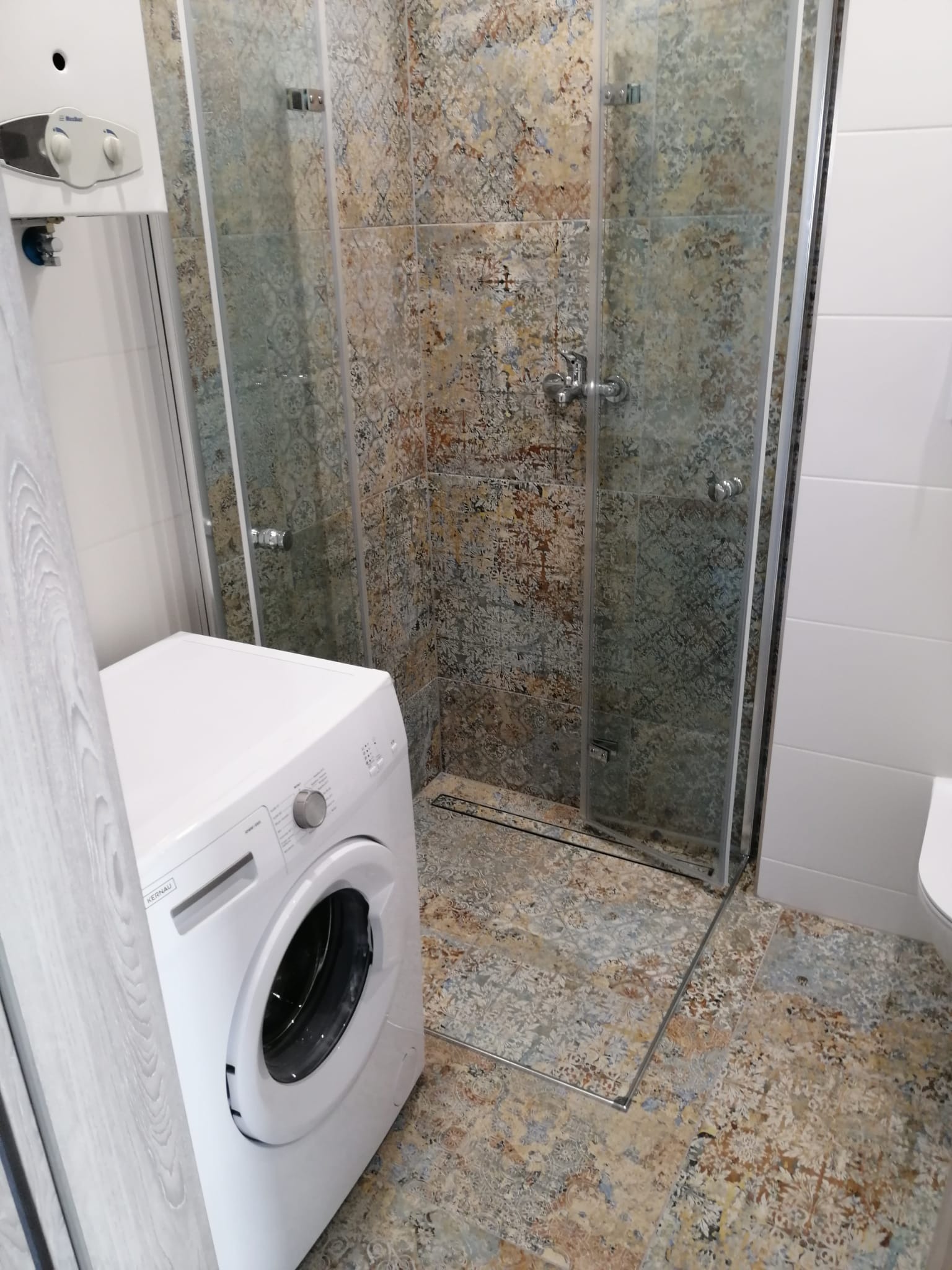 Ukończona łazienka z kabiną prysznicową typu walk-in, wzorzyste płytki na ścianach i podłodze, biała pralka Kernau w rogu.