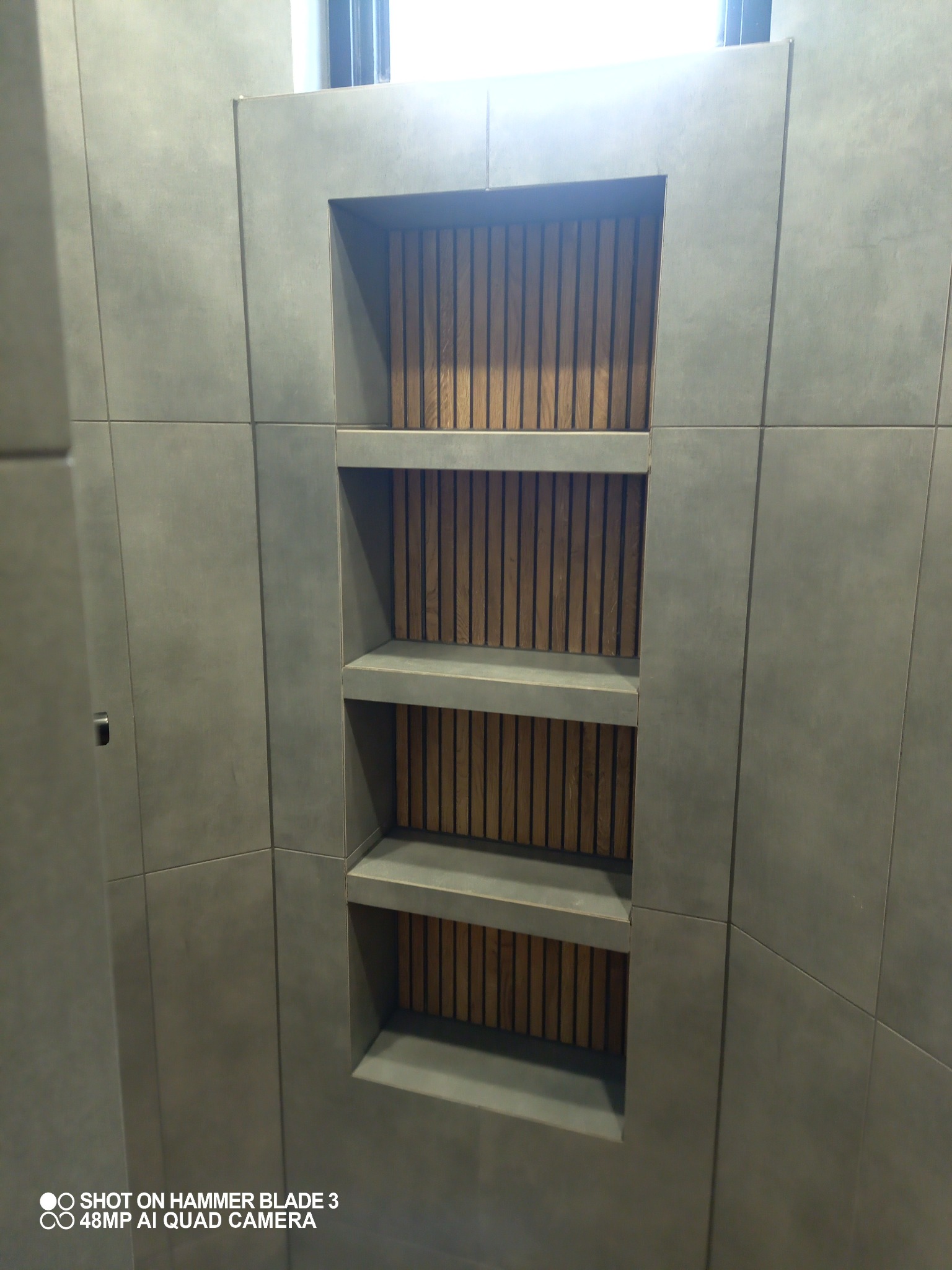 Wnęka z drewnianą okładziną w szarej, płytkowej ścianie łazienki, widok z dołu.