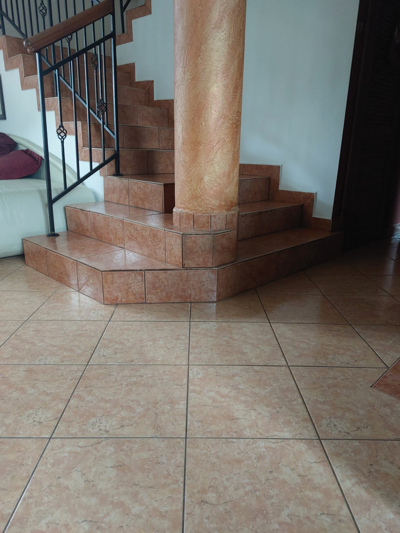 Wykończone schody z terakoty w odcieniach beżu i brązu, z metalową balustradą. Podłoga również wyłożona tą samą terakotą. Dekoracyjny filar przy schodach.