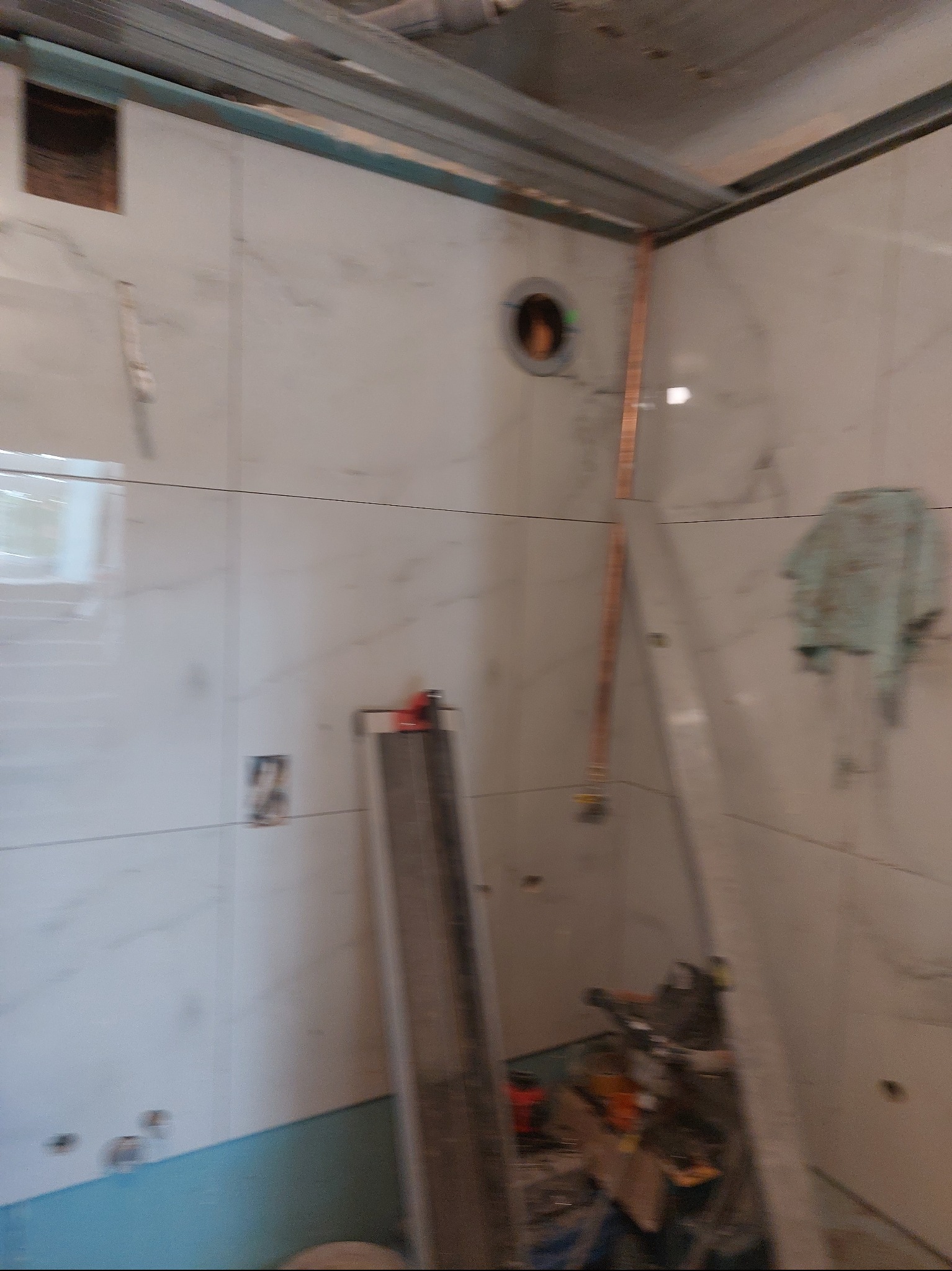 Białe, marmurowe płytki ścienne w trakcie montażu w łazience. Widoczne narzędzia i elementy instalacji. Metalowa konstrukcja sufitu podwieszanego.