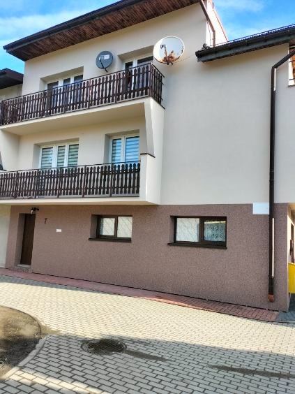 Dwupiętrowy dom z balkonami i elewacją w odcieniach beżu i brązu, widoczne dwie anteny satelitarne na górnym balkonie.