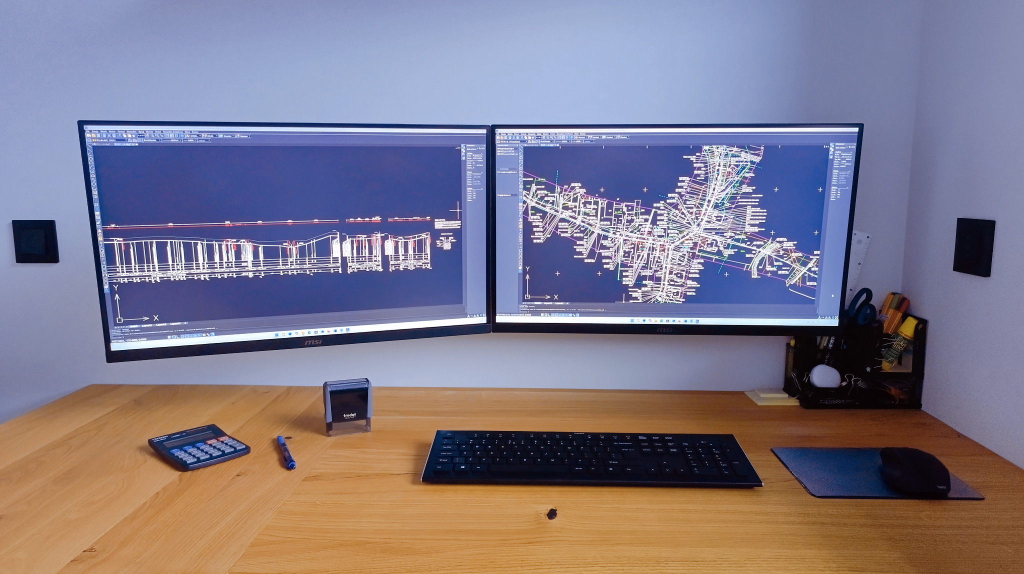 Dwa monitory wyświetlające schematy instalacji; na biurku kalkulator, pieczątka Trodat, klawiatura i myszka.