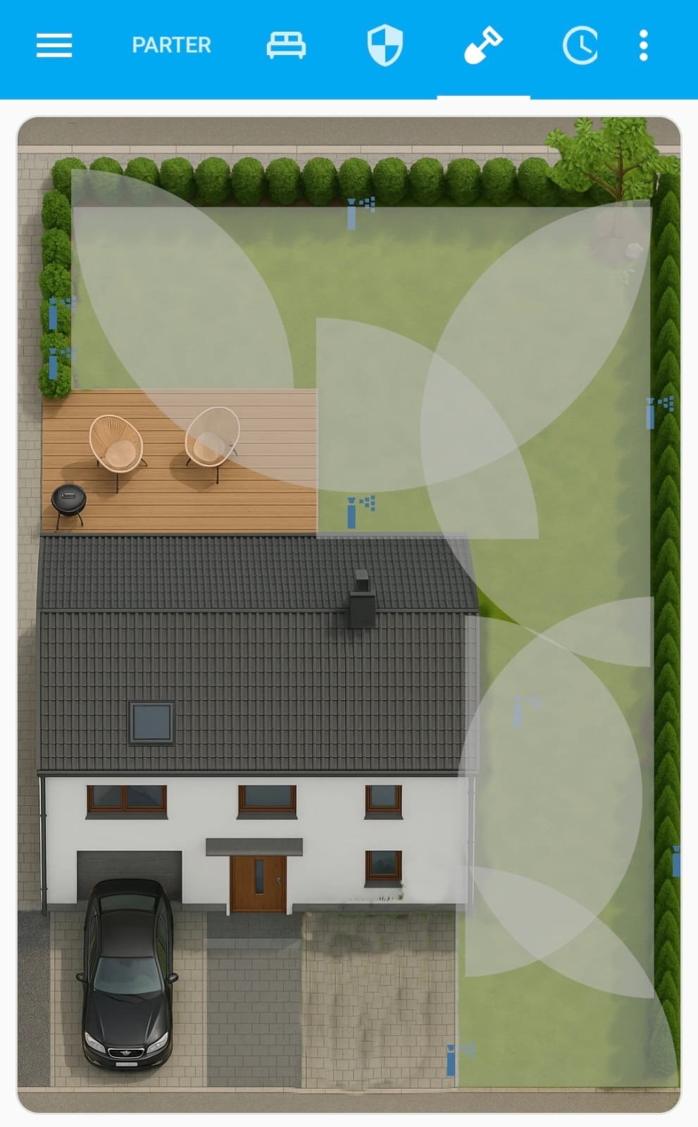 Plan domu z ogrodem widziany z góry, z zaznaczonymi strefami nawadniania. Widoczny taras z meblami ogrodowymi, trawnik, krzewy i zaparkowany samochód.