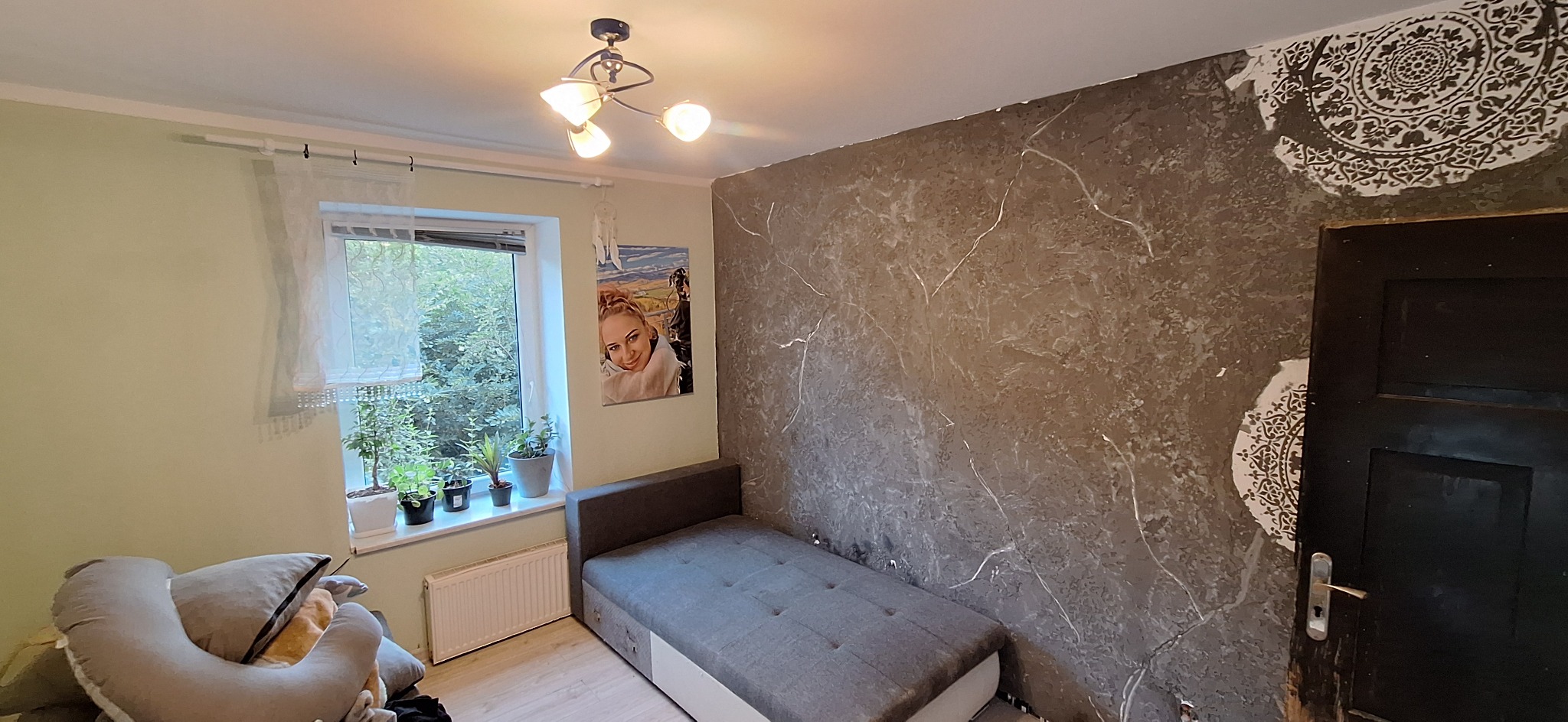 Pokój po szpachlowaniu i malowaniu dekoracyjnym ścian z efektem marmuru. Widoczny fragment wzoru na ścianie przy czarnych drzwiach i łóżko w pokoju.