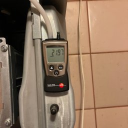 SOUNDHEISS SPÓŁKA Z OGRANICZONĄ ODPOWIEDZIALNOŚCIĄ - Miernik ciśnienia gazu Testo 510 przy piecu gazowym, wskazujący odczyt 21.97 mbar, podczas serwisu. Widoczne elementy instalacji i płytki ceramiczne w tle.