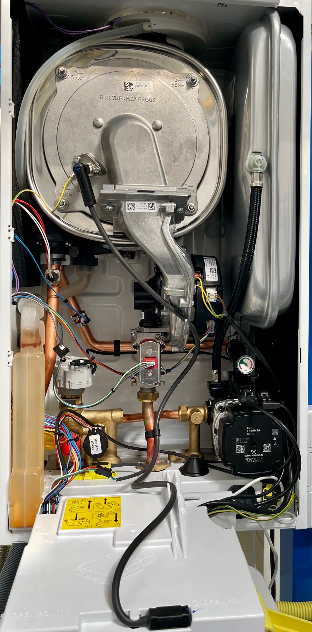 Wnętrze nowoczesnego pieca gazowego BDR Thermea Group z widocznymi komponentami: pompą Grundfos, miedzianymi rurami i okablowaniem. Detal techniczny urządzenia.