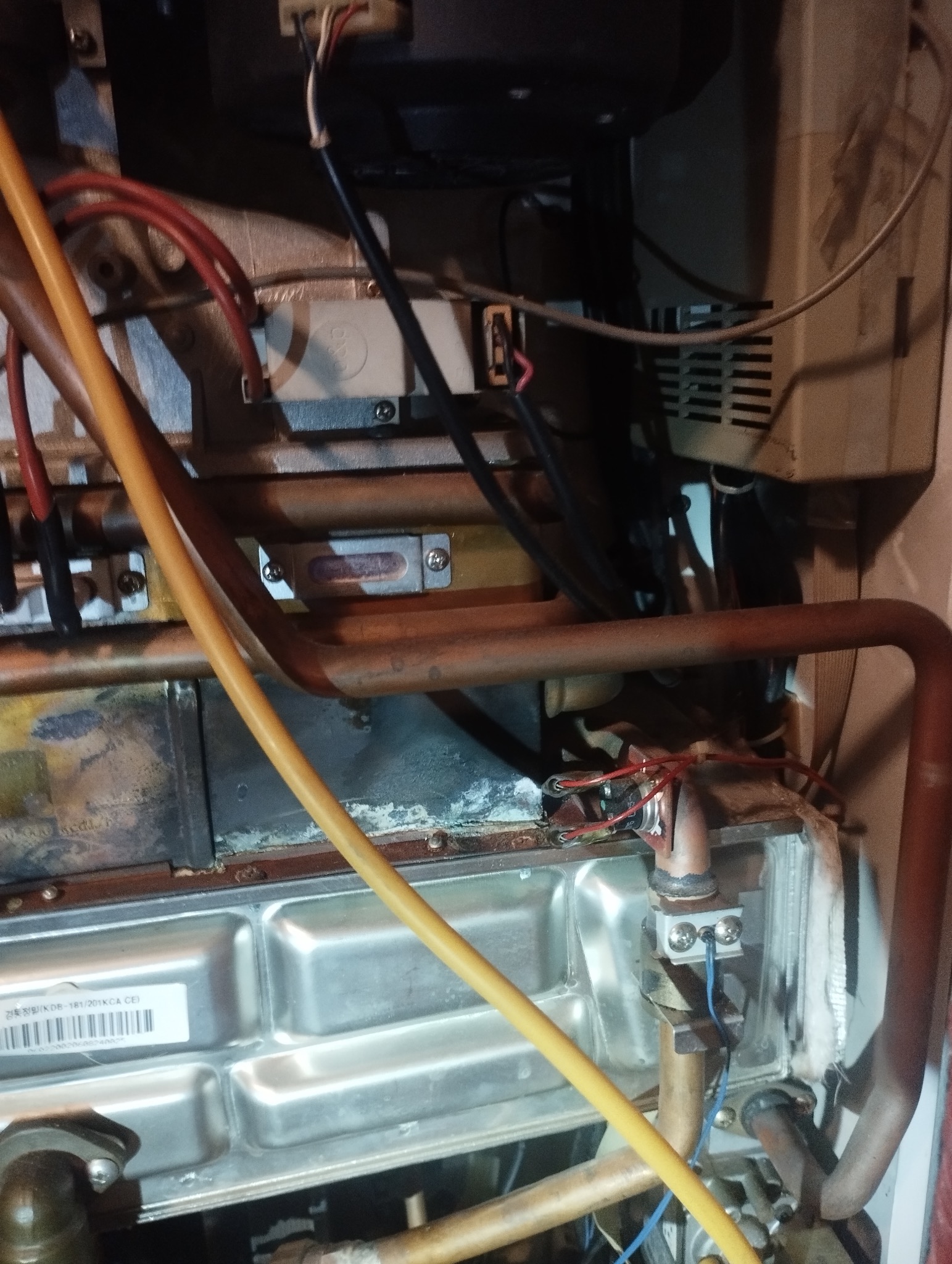 Wnętrze pieca gazowego z widocznymi przewodami, rurami i elementami elektrycznymi. Detal prezentuje skomplikowaną konstrukcję urządzenia grzewczego.