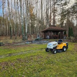 Usługi ogrodnicze Trzeciak Jakub - Żółto-biała kosiarka samojezdna Cub Cadet na trawniku z opadłymi liśćmi, w tle drewniana altana i las brzozowy.