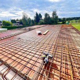 LUXHOUSE - Usługi budowlane Mariusz Kryger - Zbrojenie stropu domu jednorodzinnego z użyciem wiązarki automatycznej. Widoczne pręty zbrojeniowe ułożone na szalunku, narzędzie do wiązania drutu i elementy mocujące.